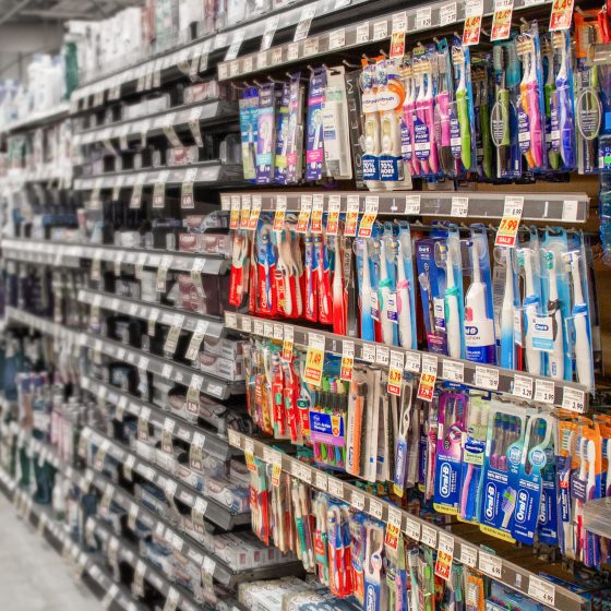 Gondola peg hook bar fully stocked with toothbrush blister packs, UPC visor labels, and organized facings on a grocery store aisle.